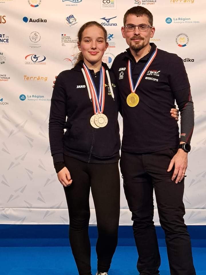 Michaël et Lucy portant leurs médailles devant le panneau des Championnats de France